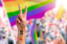 Supporting Hand Makes Peace Sign In Front Of A Rainbow Flag Flying On The Sidelines Of A Summer Gay Pride Parade With Copy Space