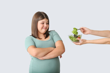 Wall Mural - Offering of healthy vegetable salad to displeased overweight girl on light background