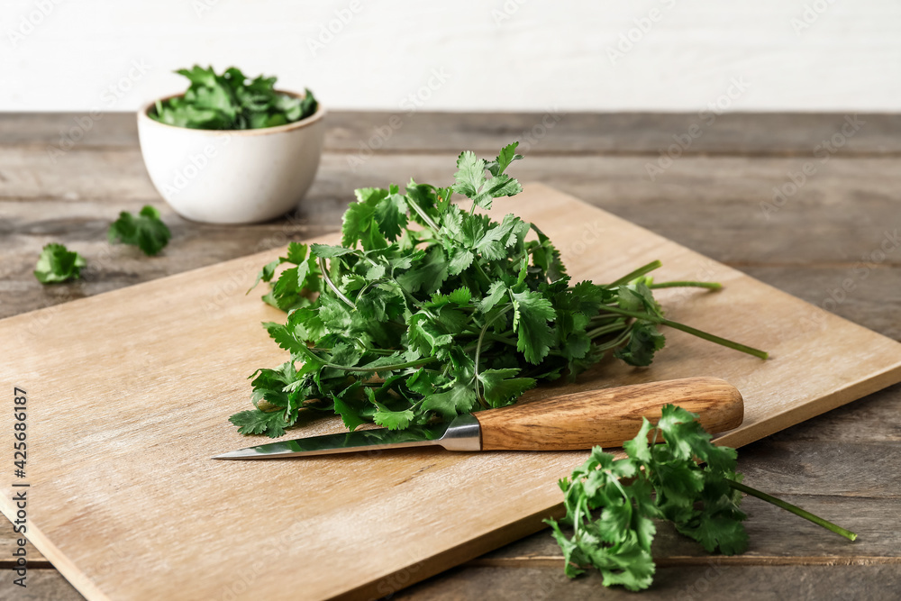 Board with fresh cilantro and knife on wooden table