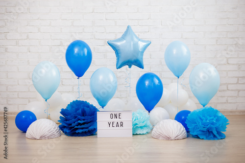 Obraz Dibond baby boy first birthday party decoration - air balloons, paper balls and lightbox with one year text over brick wall