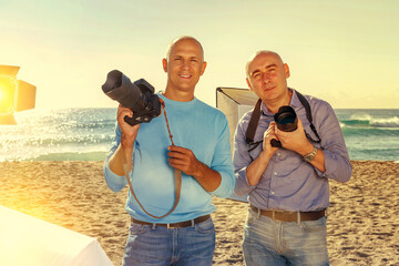 Portrait of two happy successful photographers with their cameras during professional photo shooting on sea coast