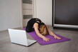 © Aleksandra Iarosh - young woman doing asana at home on yoga mat in front of laptop