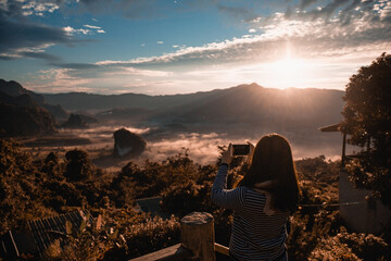 The girl take photo with smart phone on balcony bar at Phu Lang Ka mountain landmark in Phayao province Thailand.