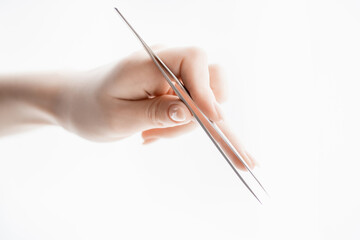 Close-up hand of master holds tools for eyebrow correction and eyelash extension tweezers and tongs on white background