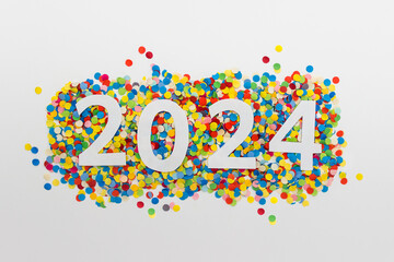 New year 2024 number made of white paper arranged on colorful confetti on white paper.