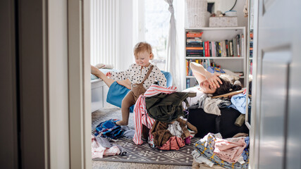 tired mother with small toddler daughter in messy bedroom at home, resting.