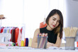 © Bangkok Click Studio - Smiling Asian woman dressmaker is sitting  sketch dress that she has to cut for the customer in the Tailor shop. Concept creating new clothes collection.