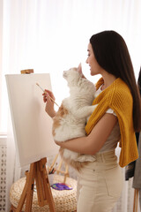 Poster - Beautiful young woman drawing on easel with cat at home