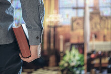 Man Holding Holy Bible In Church With Alter In Background