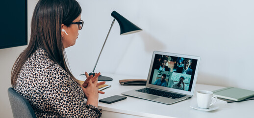 Wall Mural - Businesswoman talking on video call meeting with colleagues. Business woman discuss with coworkers at online web conference using a laptop and bluetooth earphones, sitting at desk working at home