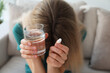 Upset young woman with abortion pill and glass of water at home, focus on hands