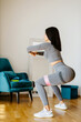 © shevtsovy - Young sporty woman doing squat morning exercise. home fitness routine. Woman with strong glutes workout at home. Female gymnastics. Butt workout motivation.