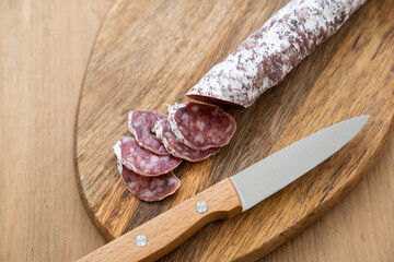 Raw smoked sausage cut into pieces and a knife on a wooden cutting board