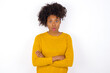 © Roquillo - Shocked embarrassed young beautiful African American woman wearing yellow sweater against white wall keeps mouth widely opened. Hears unbelievable novelty stares in stupor