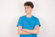 © Roquillo - Charming thoughtful young caucasian handsome man with curly hair wearing blue T-shirt against white studio wall stands with arms folded concentrated somewhere with pensive expression thinks what to do