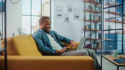 Aufkleber - Handsome Black African American Man Working on Laptop Computer while Sitting on a Sofa in Cozy Living Room. Freelancer Working From Home. Browsing Internet, Using Social Networks, Having Fun in Flat.