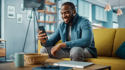 Aufkleber - Excited Black African American Man Having a Video Call on Smartphone while Sitting on a Sofa in Living Room. Happy Man Smiling at Home and Talking to His Friends and Family Over the Internet.