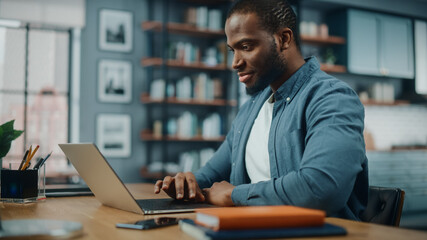 Aufkleber - Handsome Black African American Man Working on Laptop Computer while Sitting Behind Desk in Cozy Living Room. Freelancer Working From Home. Browsing Internet, Using Social Network, Having Fun in Flat.