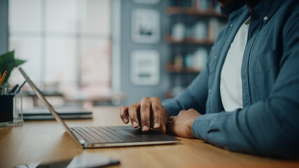 Wall Mural - Close Up on Hands of a Black African American Man Working on Laptop Computer while Sitting Behind Desk in Cozy Living Room. Freelancer Working From Home. Browsing Internet, Using Social Network.