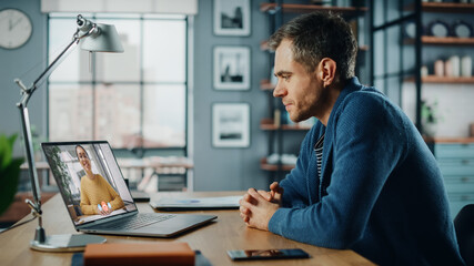 Aufkleber - Handsome Caucasian Man Having a Video Call on Laptop Computer while Sitting Behind Desk in Living Room. Freelancer Working From Home and Talking to Colleagues and Clients Over the Internet.