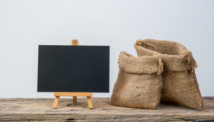 Black board stand and two different size burlap bags on grunge wooden  shelf with copy space isolated over white background