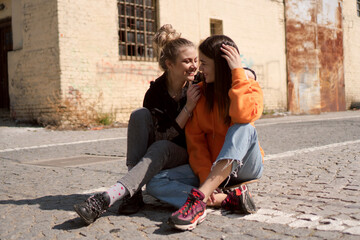 Two teenage skater girls are hanging out in the neighborhood, chatting and smiling.