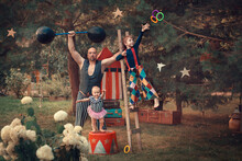 Family Portrait In Vintage Circus Style. Father Is Dressed As A Strongman With Barbell, Son Is Dressed As Clown And Baby Daughter Is Dressed As Pretty Assistant. Image With Selective Focus And Toning