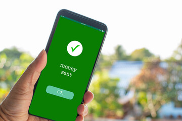 A man's hand holds a smartphone on the screen with the message money sent. Concept of financial transactions with mobile devices. Closeup, copy space on right for design or text. blurred background.