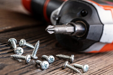 wooden background, retro style, grunge. Green screwdriver and in the box there are black and silver self-tapping screws. Close-up.