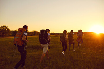 Wall Mural - group of five people with large backpacks move in a row across a field at sunset.