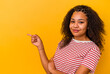 Young african american woman isolated on yellow background smiling cheerfully pointing with forefinger away.