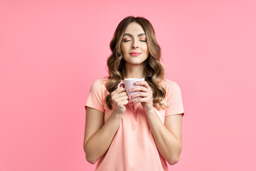 Wall Mural - Young pretty woman enjoying cup of aroma coffee closed eyes on pink background