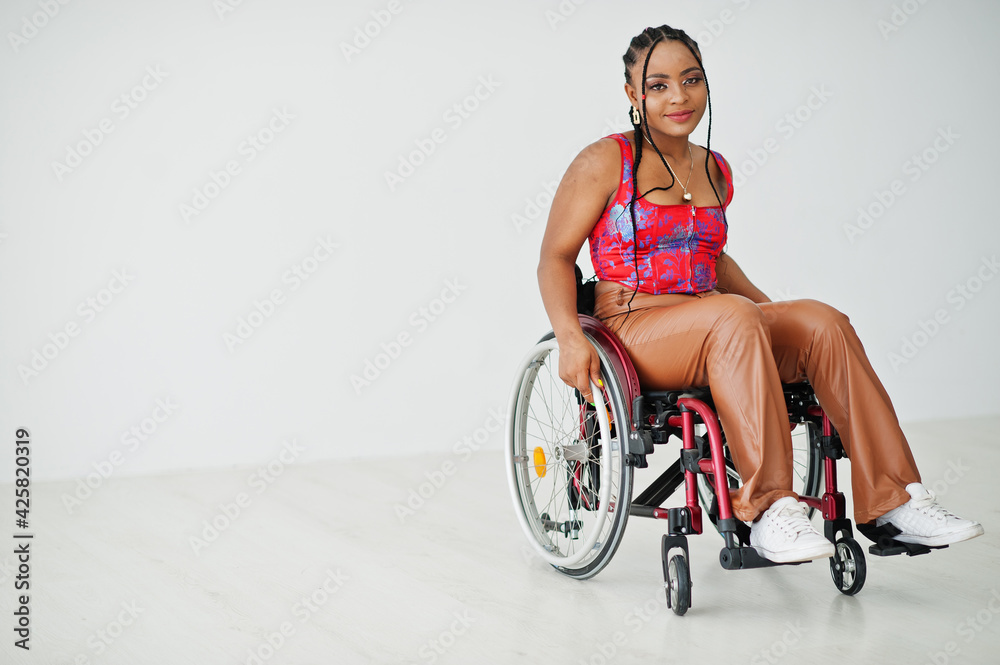 Young disabled African American woman in wheelchair against white wall. - obrazy, fototapety, plakaty 