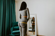 © shevtsovy - Smiling Woman Measuring body With Tape Standing In Front Of Mirror At Home. Beautiful fitness woman checking success of weight loss program and measuring butt in front of mirror in living room