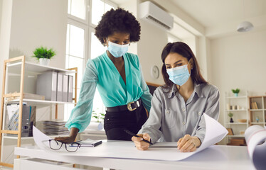 Wall Mural - Safety during coronavirus pandemic. People in face masks work in office studio after end of lockdown and quarantine. Two creative designers and business women thinking and making poster or draft plan