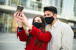 Young couple taking a selfie portrait together outdoor and wearing masks to prevent coronavirus covid 19 pandemic