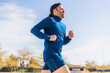 © AntonioJavier - A young white european and athletic man is running in the street on a sunny day. The guy is wearing blue clothes and a cap.