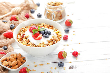 Tasty granola with fresh berries and almonds on white wooden background