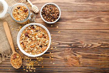 Poster - Tasty granola in bowls, glass jar and spoon on brown wooden background