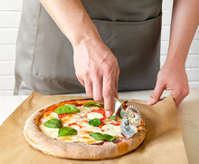 Closeup Hand Of Chef Baker In Grey Uniform Cutting Pizza At Kitchen