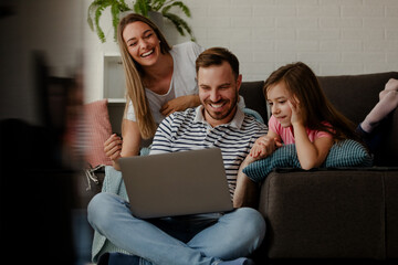 Wall Mural - Young smiling family is watching funny videos on laptop computer. Happy family time.