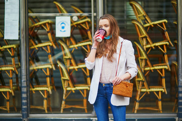 Young girl standing near closed restaurant in Paris and wearing protective face mask during coronavirus outbreak