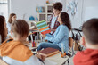 © Ivan - Young teacher reading with her student in front of whole class. Elementary school kids sitting on desks and reading books in classroom