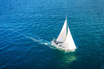 Regatta sailing ship yachts with white sails at opened sea. Aerial view of sailboat in windy condition.