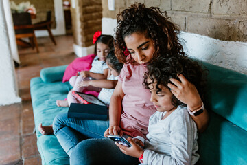 Wall Mural - latin mother on sofa at home with little boy child use phone browse Internet together in Mexico city