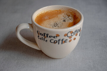 A cup of coffee in the morning light with an appetizing froth on a ceramic gray surface.