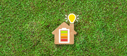 Energy efficiency and rating chart in a small model house with glowing lightbulb in the chimney over green grass in an ecological and environmental concept