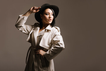 Pretty young woman in white coat and hat posing on brown background