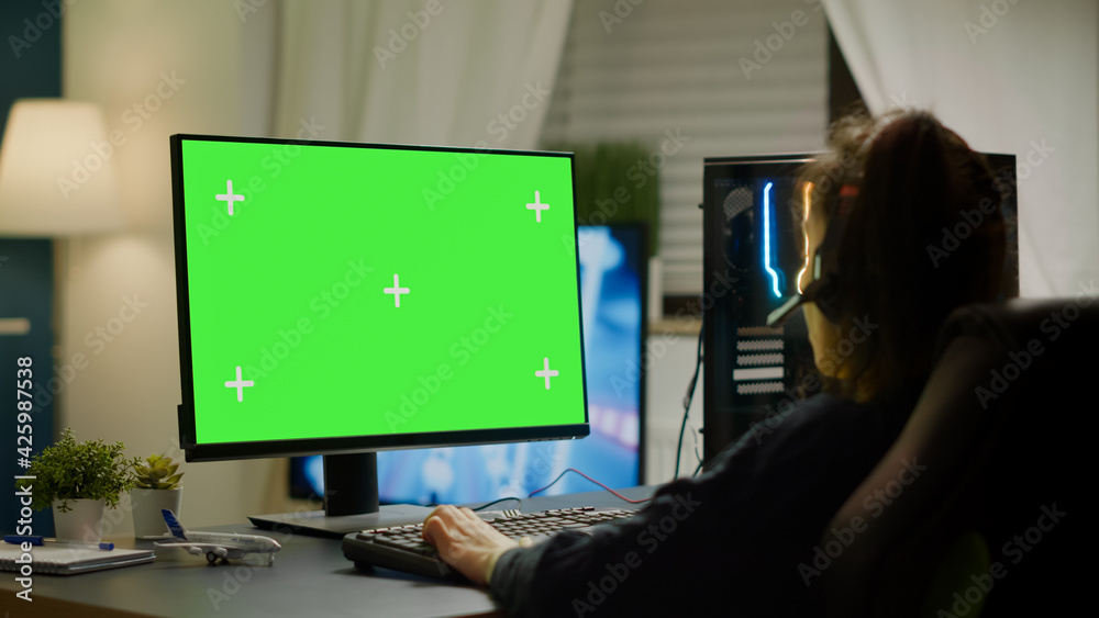 Pro gamer playing virtual video game on powerful computer with green screen mock up, chroma key display. Cyber player using professional pc with isolated desktop streaming shooter games wearing - obrazy, fototapety, plakaty 