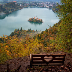 Wall Mural - Wooden bench with fantastic view to the famous alpine Bled lake (Blejsko jezero), island with church, mountains and sky, amazing autumn landscape, outdoor travel background, Slovenia